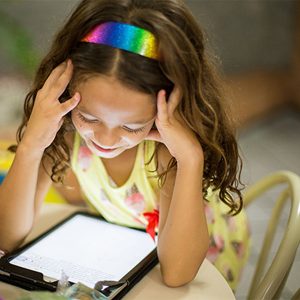 Girl reading digital book with rainbow headband in a reading nook.